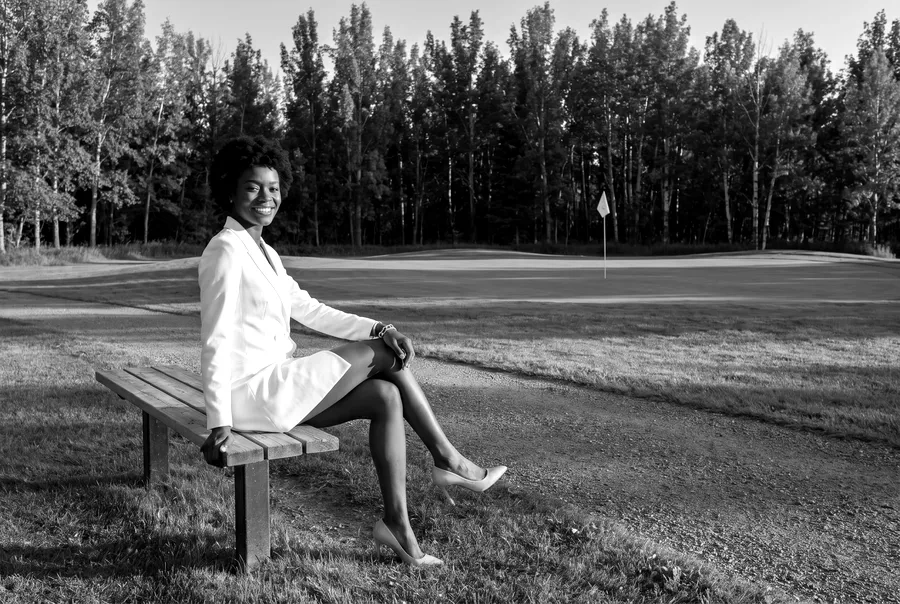 A woman in white on a bench by a golf green