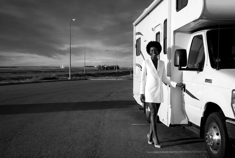 Woman beside a white motorhome on a paved lot at dusk